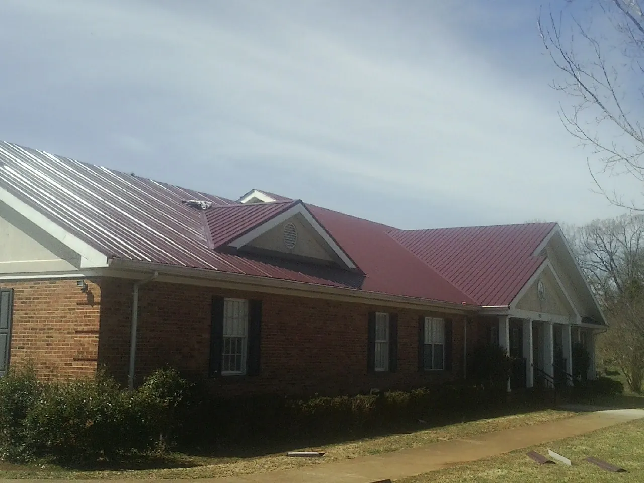 Red metal roof with gabled entries on a long brick building, from a Hail Damage Roof Repair job in Fairfax Station