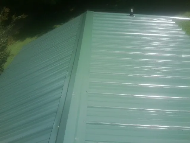 New green metal panels meeting at the ridge of a roof — Flat Roof Repair work by our crew in Fairfax Station