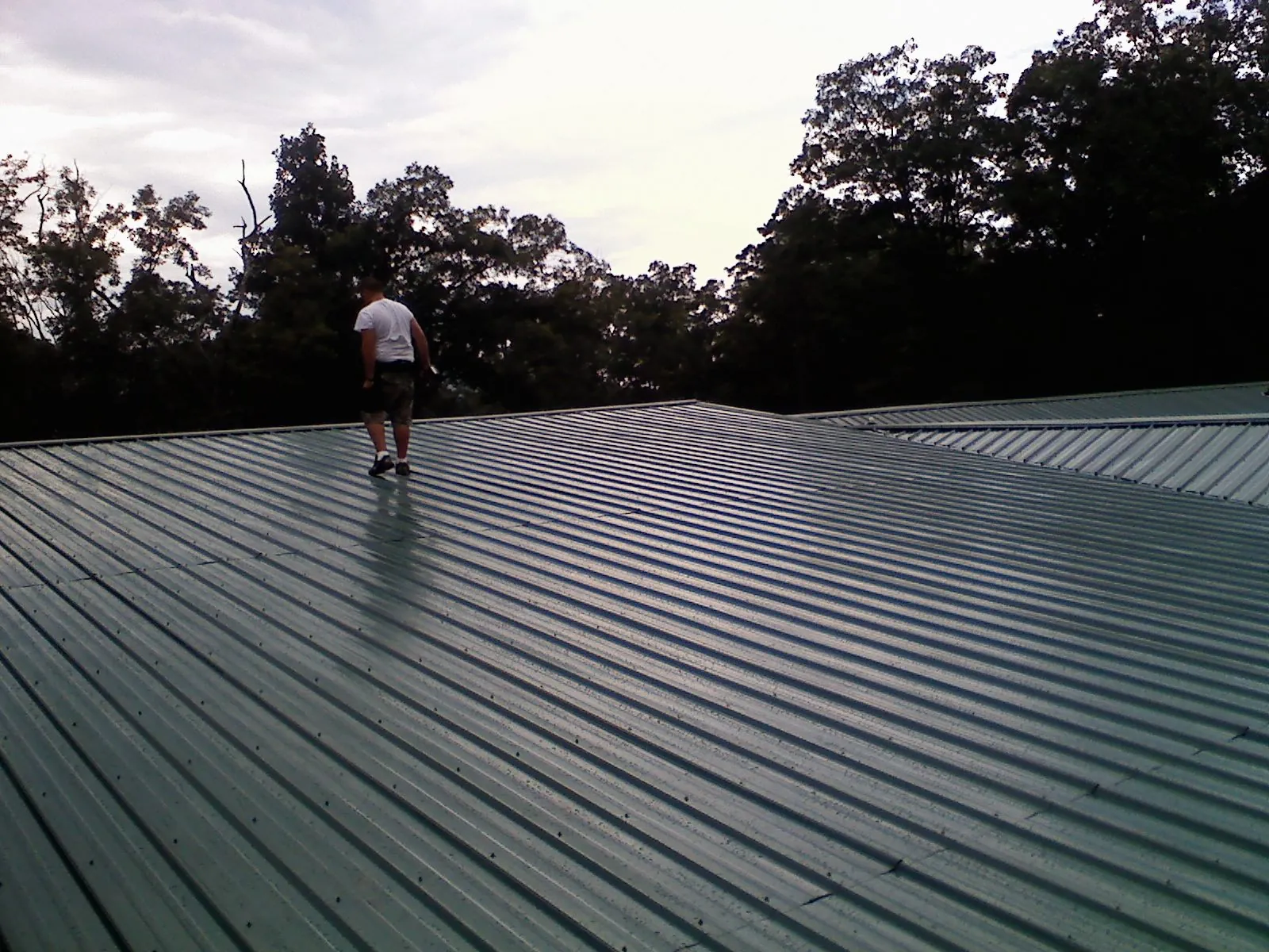 Roofer walking a wide expanse of new green metal roofing in Fairfax Station