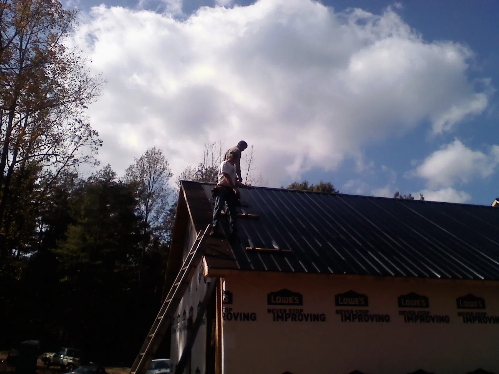Roofer fastening dark metal panels high against a cloudy sky, from a Roof Inspection job in Fairfax Station