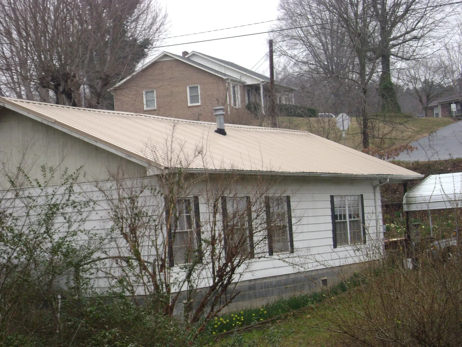 Tan metal roof on a white sided house set into a hillside — Commercial Roofing by Roofing Brothers in Fairfax Station